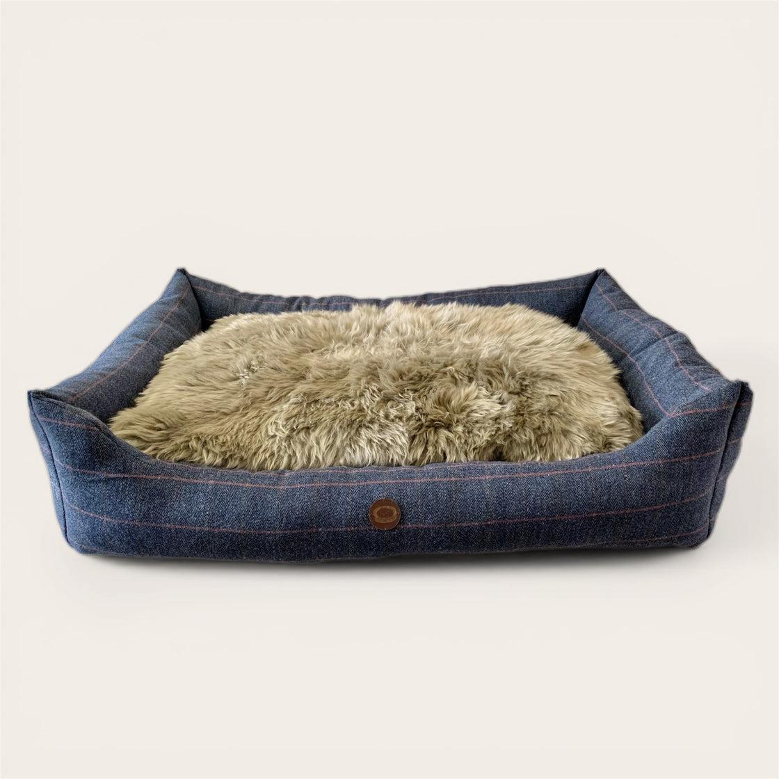 Dog bed with blue tweed exterior and beige sheepskin interior on a light background